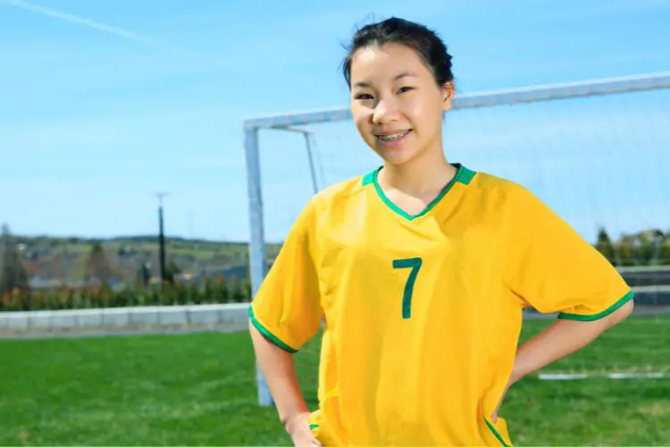 A soccer girl smiles at the camera on a bright sunny day on the soccer field