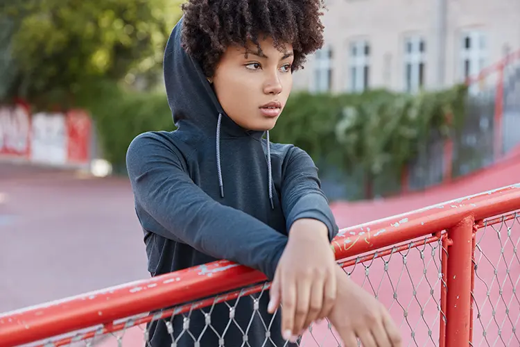 Black teenage girl with a hoodie on her head leaning on a fence