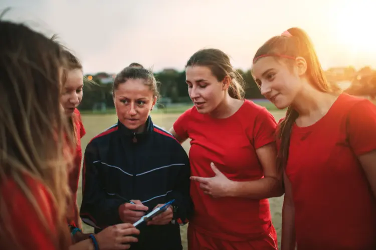 Soccer coach talking with her team on the field at sunset