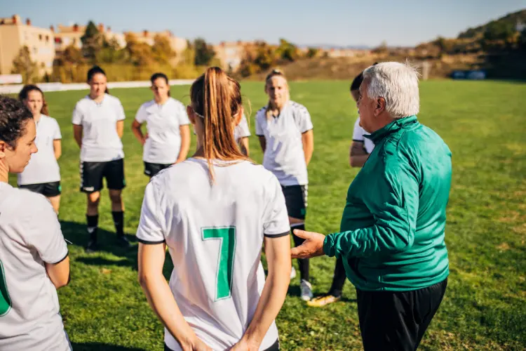 High school soccer coach talks with his female soccer team out on the field before practice