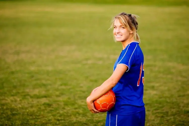 Female soccer player smiles at the camera while holding a soccer ball