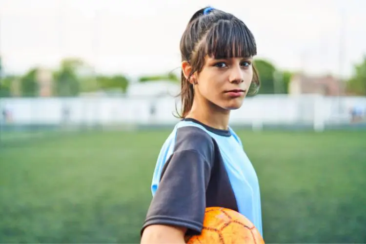 Female soccer player looking at the camera seriously while holding a soccer ball