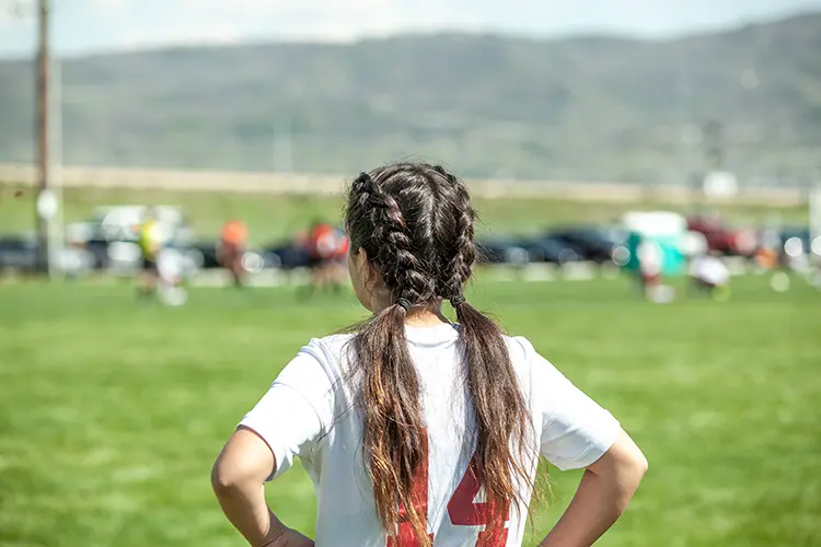 Female soccer player with her hair in two braids standing with her hands on her hips during a soccer game
