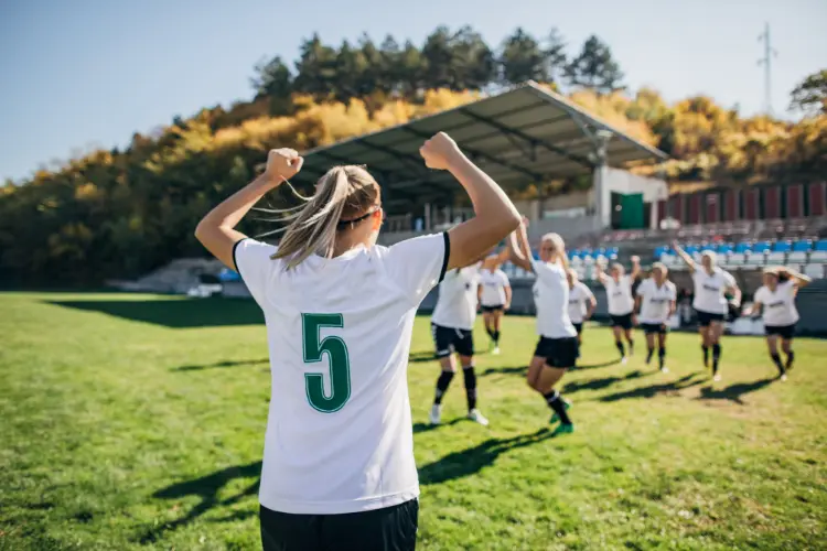 Women's soccer player pumping her fists in the air in excitement after scoring a goal