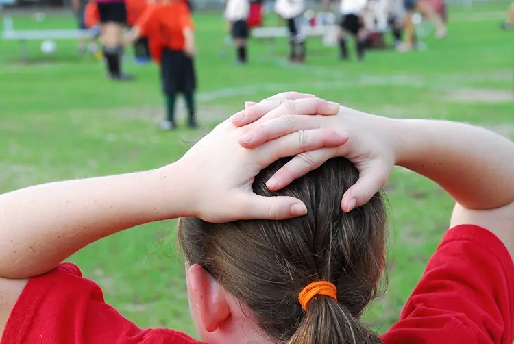 Young girl with her hands on her head watching a soccer game