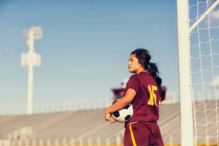 Portrait of a female soccer player looking off into the distance with empty stadium bleachers and a blue sky in the background