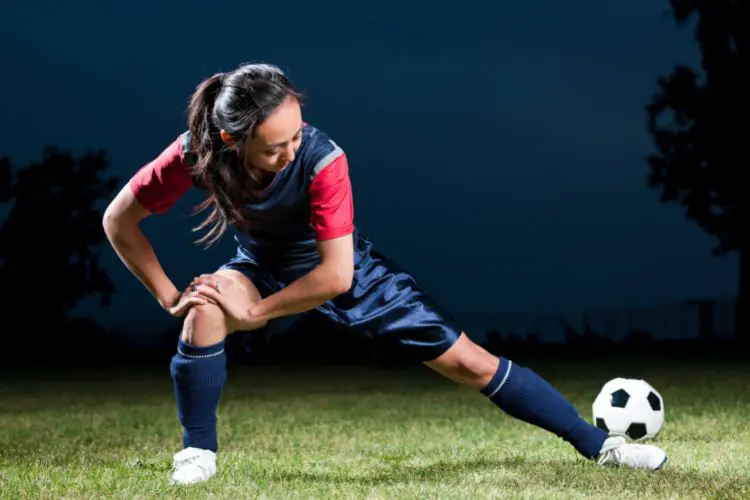 A soccer players stretches on her own before a late night training session