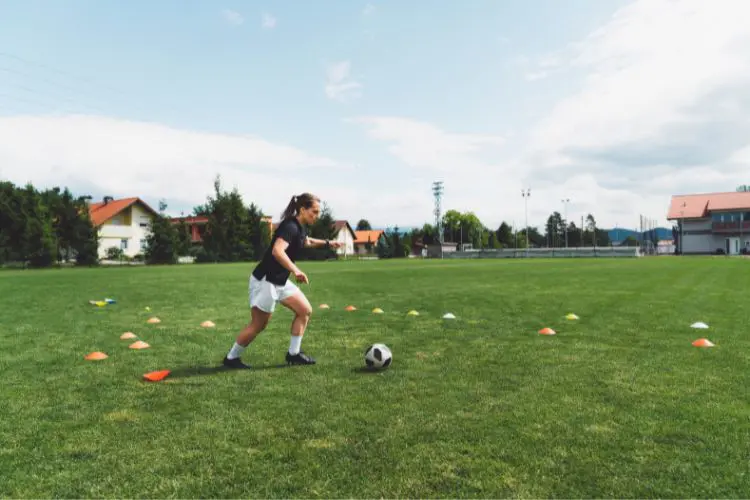 Female soccer player individual training with cones in a grass field