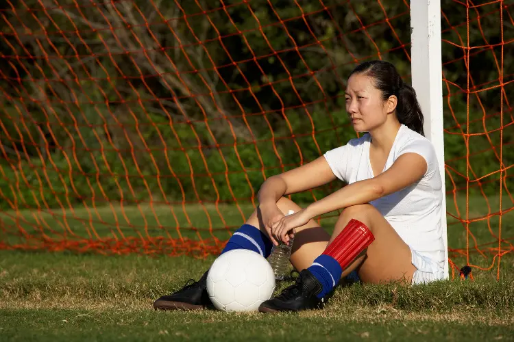 Sad soccer player sitting on the ground leaning against the goalpost