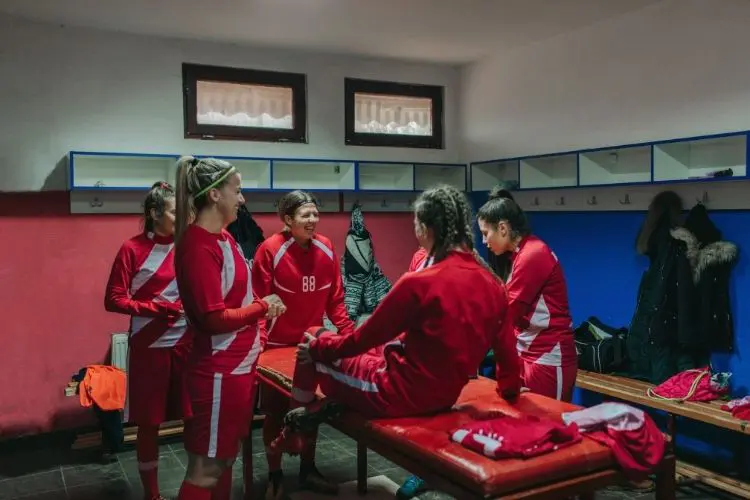 A high school girls soccer team gathers in a locker room after a game
