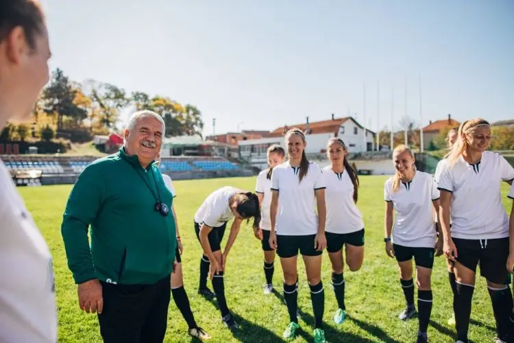 A college soccer coach smiles and laughs with his team