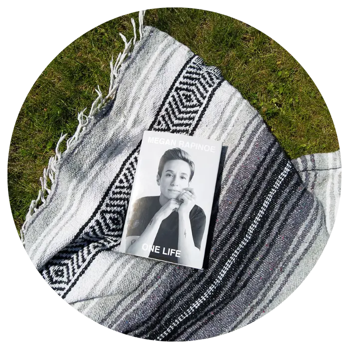 Megan Rapinoe's book One Life sitting on a blanket in the grass