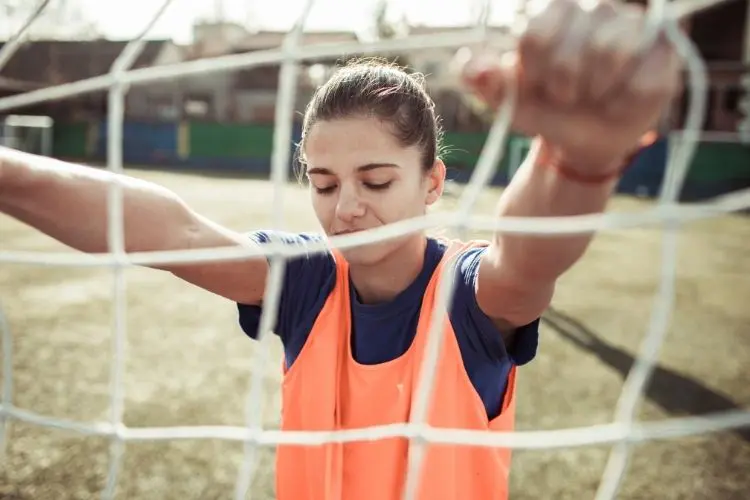 A soccer player grabs the net in a way that looks as if she is stressed out and experiencing negative self-talk