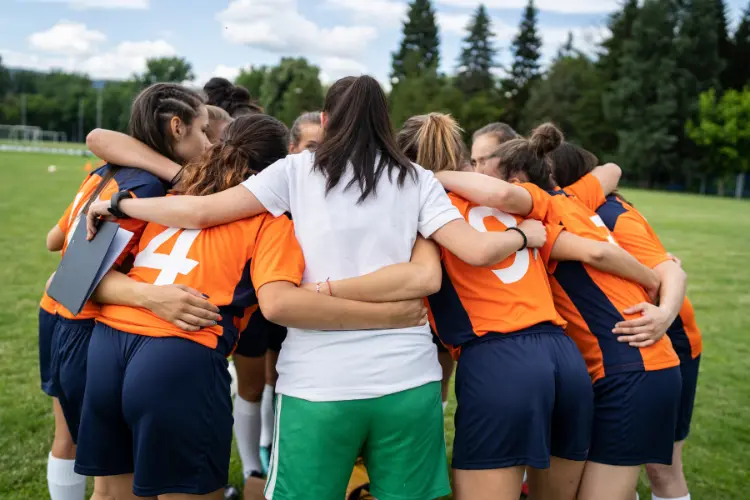 Team in orange huddled up with their coach before the start of a soccer game