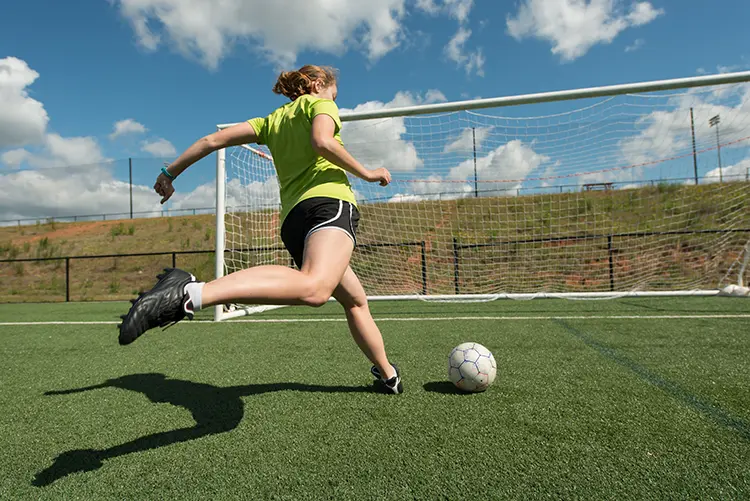 Girl shooting a soccer ball on an empty net during shooting training