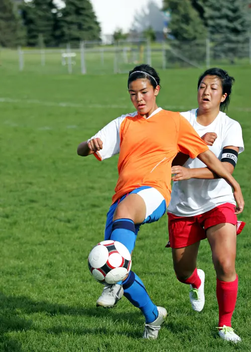 A soccer player reaches for the ball while another player pushes her from behind during a soccer game