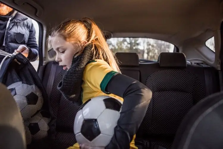 A young girl climbs out of the car before soccer practice
