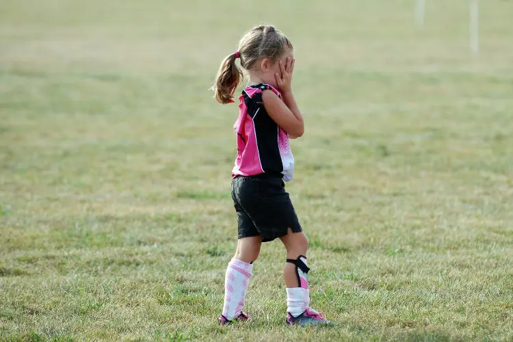 A young girl holds her hands over her face on the soccer field