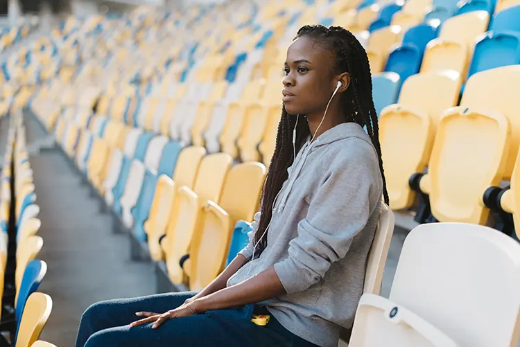 Young black woman wearing headphones and sitting in an empty stadium thinking