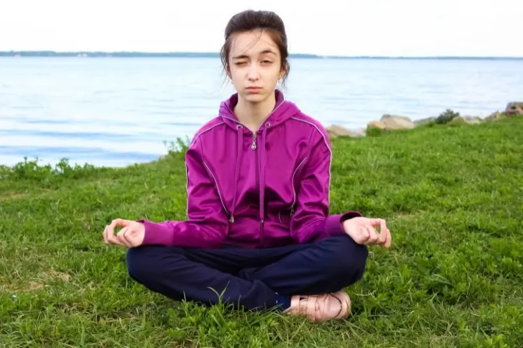 A young girl tries to meditate but is opening one eye in a skeptical way