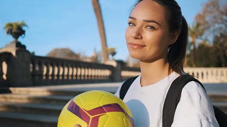 Smiling girl in a backpack holding a soccer ball