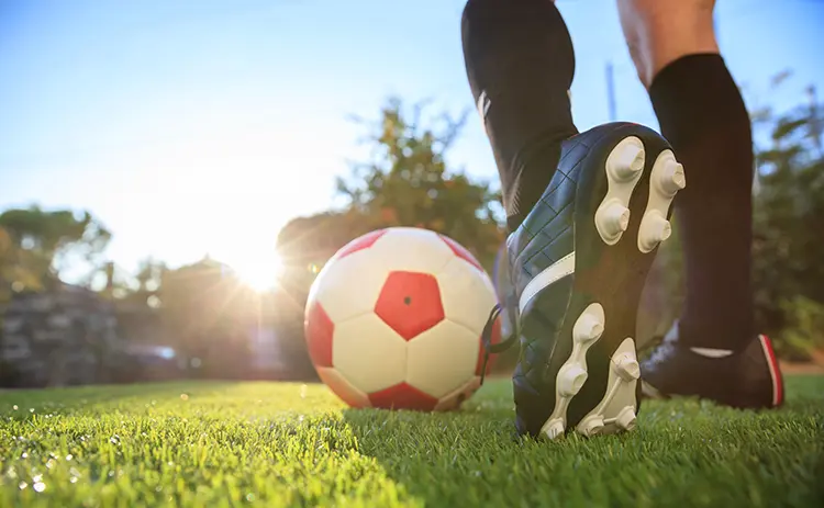Soccer player's cleats and feet with a soccer ball on a grass field