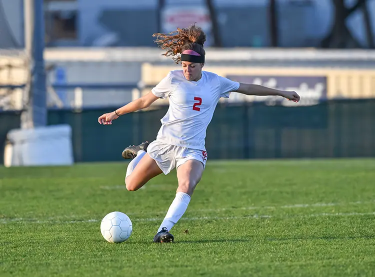 High school soccer player striking the ball on a grass field