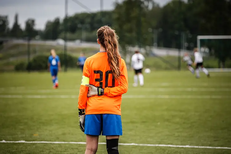 Goalkeeper with a ponytail standing and watching the game with a captains arms band on
