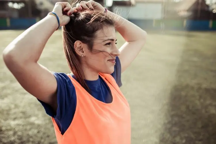 A soccer player ties her ponytail tighter while at soccer practice