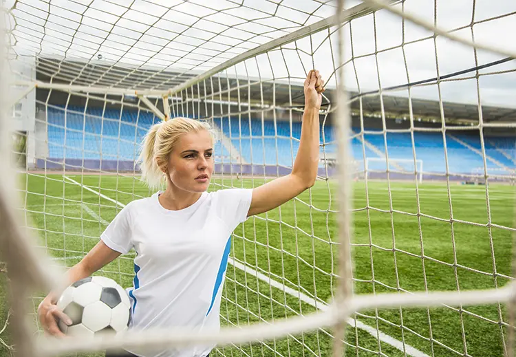 Portrait of a female soccer player holding a ball and standing inside a net