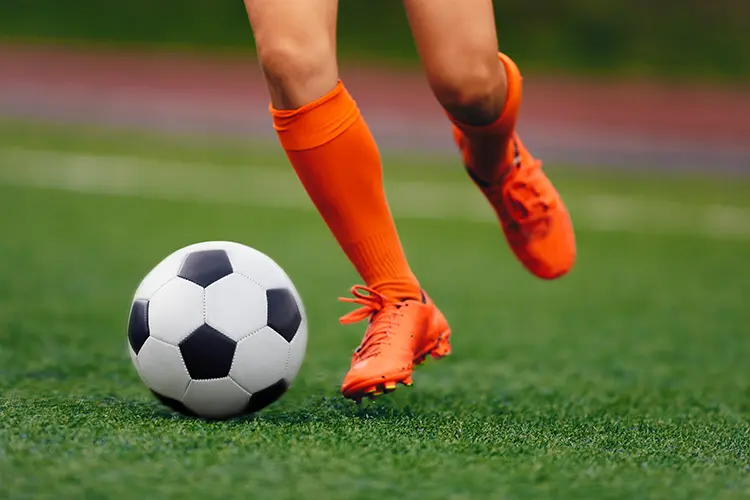 Soccer player in orange boots and orange socks dribbles up the field