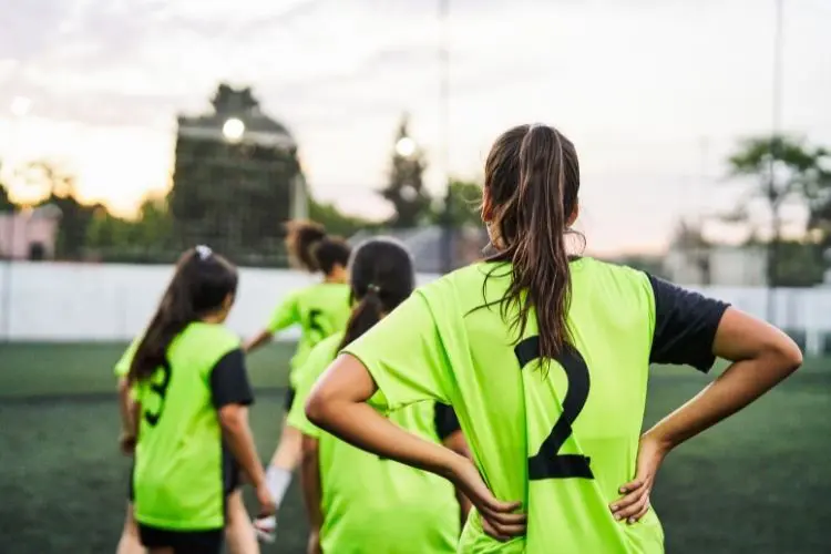 Soccer player holds her hands on her hips and looks at her teammates