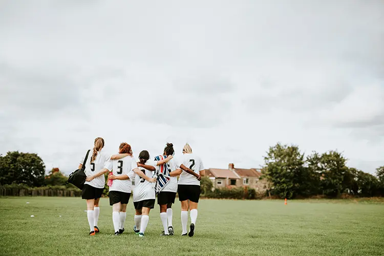 Five teenage soccer players walking off the field with their arms around each other's backs