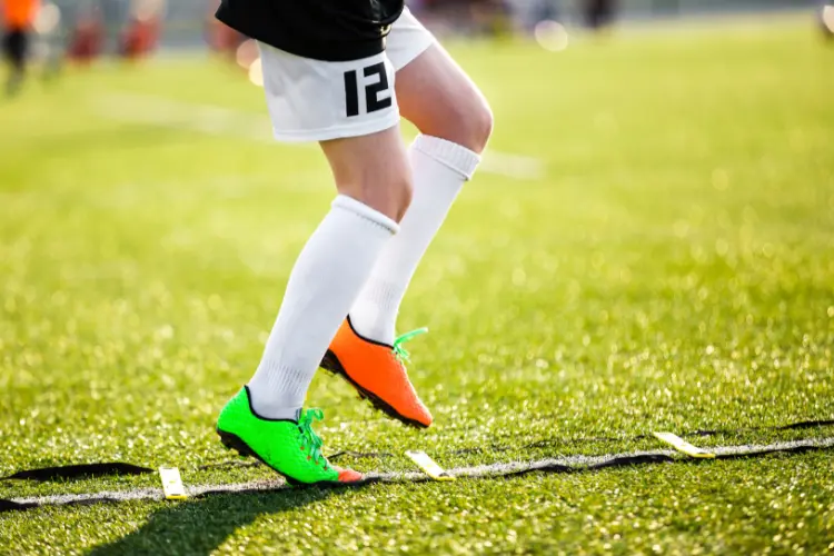 A soccer player runs up a speed ladder on a turf field to work on speed and fast feet