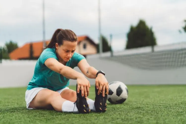 A woman stretches while sitting down on a soccer field