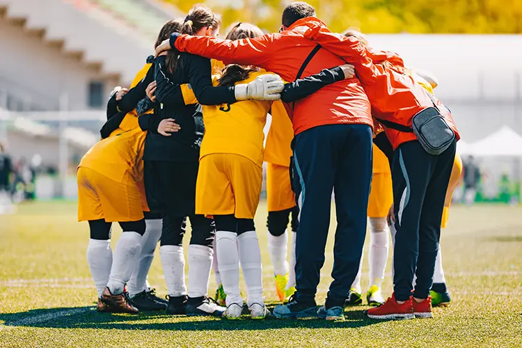 Coaching staff in a huddle with their girls soccer team before a game starts