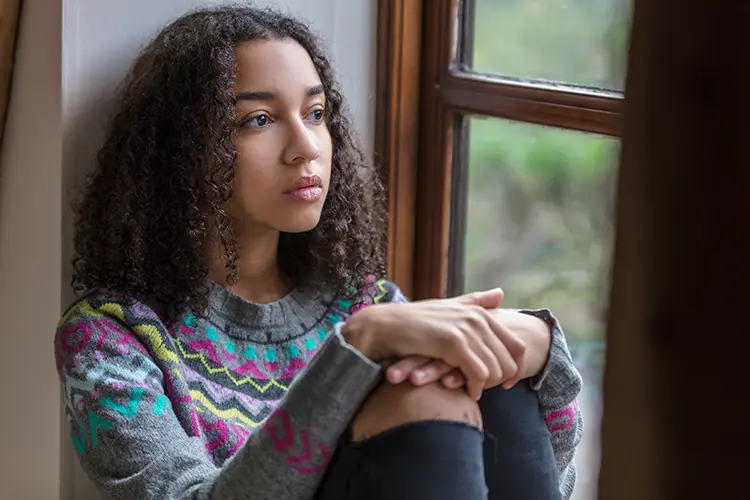Contemplative young woman in a sweater and jeans staring out the window