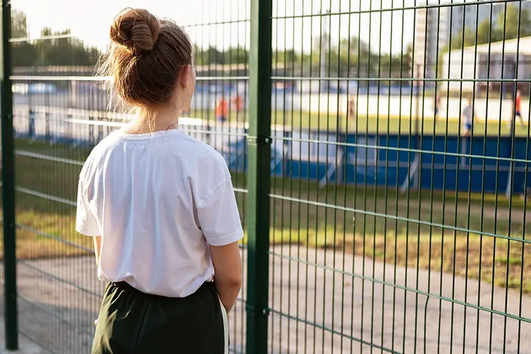 Teenage girl staring at a soccer field longingly