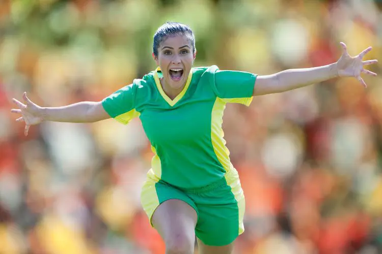 Women's soccer player shows her excitement during a football match by holding her arms out and yelling