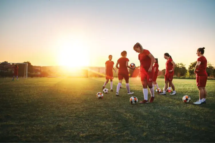 A group of players waits with their soccer balls for practice to begin with the sunset in the background