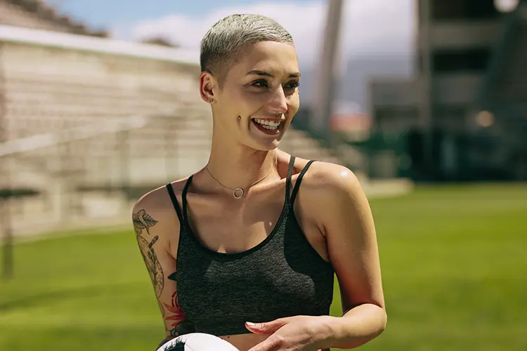 Young lady with piercings and tattoos holding a soccer ball at a stadium