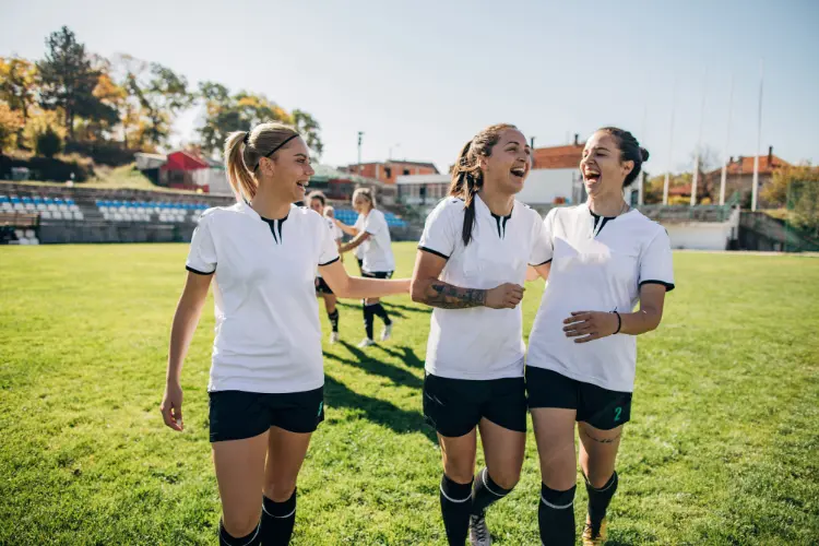 Teammates laugh and chat as they walk off the soccer field