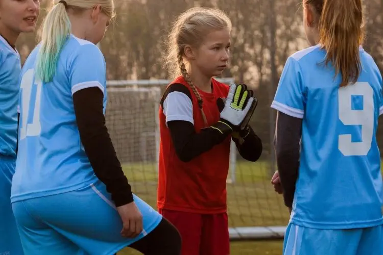 A young goalkeeper holds her hands together while she listens to her coach
